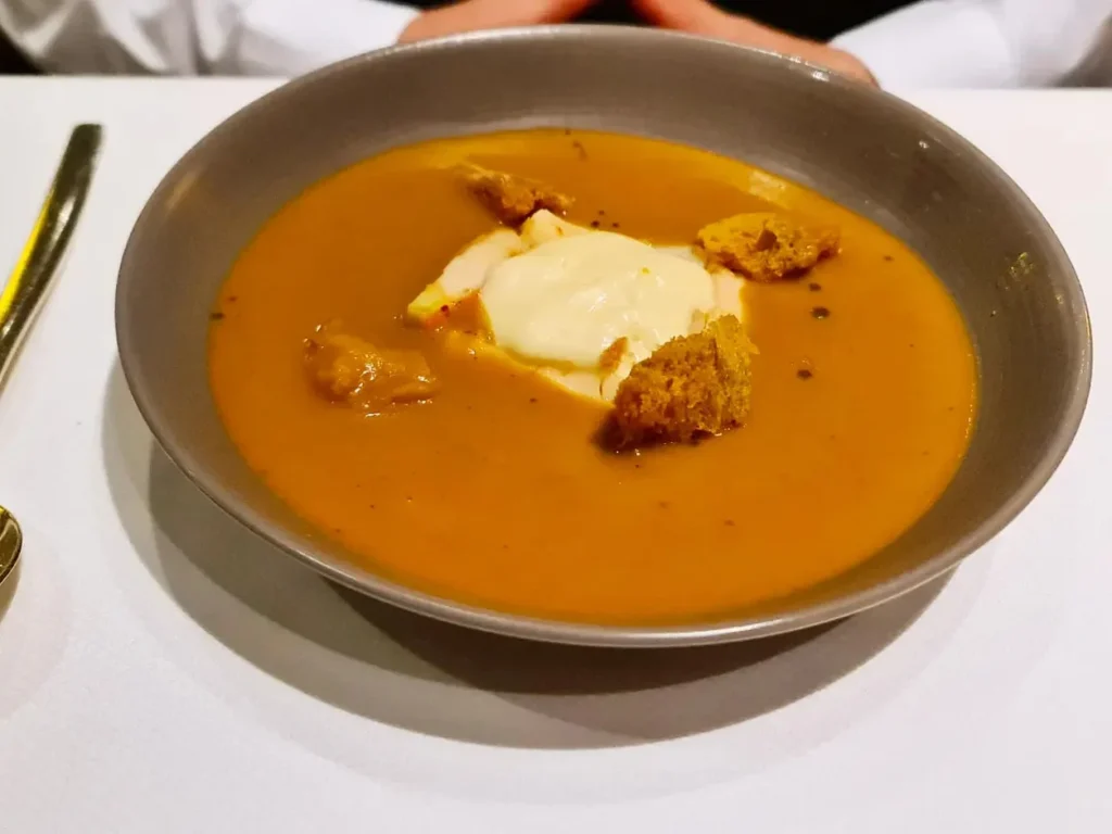 Cruising with Danny and Peter, Holland America Line, Rotterdam, Atlantic Ocean, Sea Day | A beautifully plated dish from the Taste of De Librije dinner aboard the Rotterdam, featuring Jonnie Boer cuisine, including caviar egg, king fish, and oysters, paired with Cloudy Bay Sauvignon Blanc. The elegant dining setup highlights the luxurious atmosphere of Holland America Line's Pinnacle Grill during this exquisite transatlantic cruise dinner.