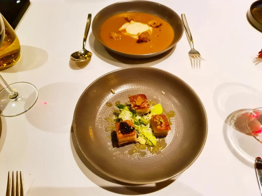 Cruising with Danny and Peter, Holland America Line, Rotterdam, Atlantic Ocean, Sea Day | A beautifully plated dish from the Taste of De Librije dinner aboard the Rotterdam, featuring Jonnie Boer cuisine, including caviar egg, king fish, and oysters, paired with Cloudy Bay Sauvignon Blanc. The elegant dining setup highlights the luxurious atmosphere of Holland America Line's Pinnacle Grill during this exquisite transatlantic cruise dinner.