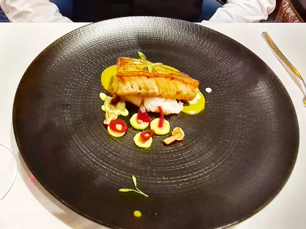 Cruising with Danny and Peter, Holland America Line, Rotterdam, Atlantic Ocean, Sea Day | A beautifully plated dish from the Taste of De Librije dinner aboard the Rotterdam, featuring Jonnie Boer cuisine, including caviar egg, king fish, and oysters, paired with Cloudy Bay Sauvignon Blanc. The elegant dining setup highlights the luxurious atmosphere of Holland America Line's Pinnacle Grill during this exquisite transatlantic cruise dinner.