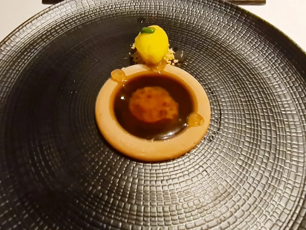 Cruising with Danny and Peter, Holland America Line, Rotterdam, Atlantic Ocean, Sea Day | A beautifully plated dish from the Taste of De Librije dinner aboard the Rotterdam, featuring Jonnie Boer cuisine, including caviar egg, king fish, and oysters, paired with Cloudy Bay Sauvignon Blanc. The elegant dining setup highlights the luxurious atmosphere of Holland America Line's Pinnacle Grill during this exquisite transatlantic cruise dinner.