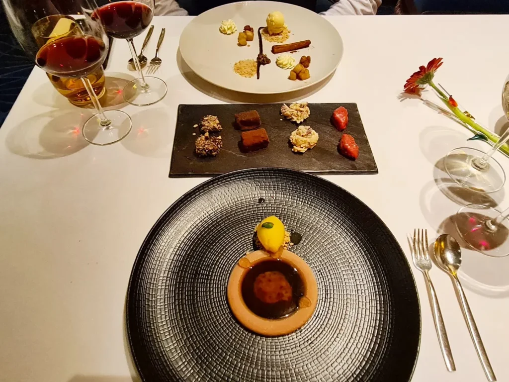 Cruising with Danny and Peter, Holland America Line, Rotterdam, Atlantic Ocean, Sea Day | A beautifully plated dish from the Taste of De Librije dinner aboard the Rotterdam, featuring Jonnie Boer cuisine, including caviar egg, king fish, and oysters, paired with Cloudy Bay Sauvignon Blanc. The elegant dining setup highlights the luxurious atmosphere of Holland America Line's Pinnacle Grill during this exquisite transatlantic cruise dinner.