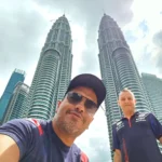 Cruising with Danny and Peter, Holland America Line, Westerdam, Port Kelang, Kuala Lumpur, Malaysia | Port Klang harbor bustling with cargo ships, vibrant staircase leading up to Batu Caves with colorful Hindu art, iconic Petronas Twin Towers towering over Kuala Lumpur’s skyline, panoramic view from KL Tower observation deck showcasing the cityscape, and historical artifacts at the National Museum illustrating Malaysia’s cultural heritage.