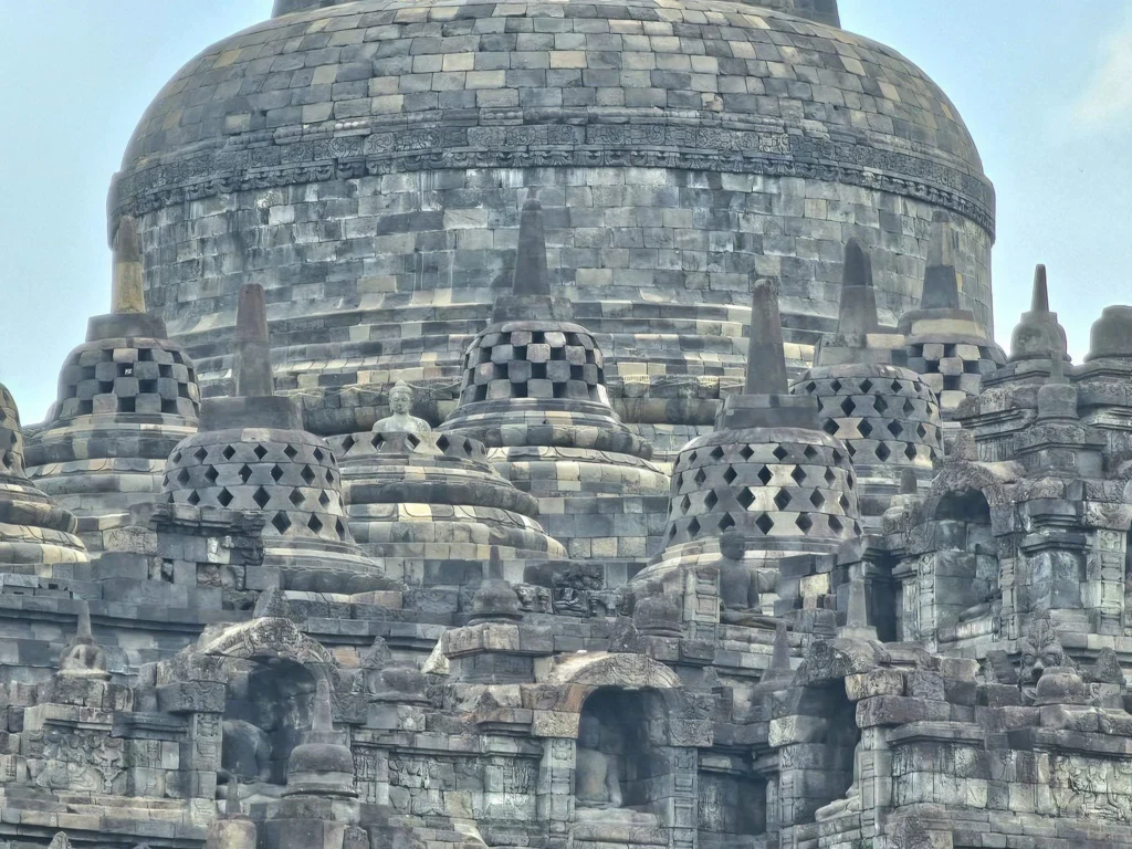 Cruising with Danny and Peter, Holland America Line, Westerdam, Semarang, Java, Indonesia, Borobudur Temple Cruise, Java Adventure | Panoramic view of Borobudur during a Borobudur Temple Cruise, showcasing the UNESCO Buddhist Temple amidst Central Java’s lush hills, with the Westerdam ship docked for the Holland America Westerdam Borobudur Tour, a Luxury Cruise Java adventure in Holland America Far East. Close-up of stupas and Buddha statues at Borobudur, reflecting Mahayana Buddhist Heritage, alongside a vibrant market scene from a Semarang Java Tour, part of an Indonesian Cultural Journey. Travelers explore this Borobudur Pilgrimage Site on a Central Java Travel excursion, enjoying a stunning sunset over the 9th-Century Temple Exploration, with detailed stone reliefs of the UNESCO Buddhist Temple and relaxation on the Westerdam deck during a Westerdam Cruise Indonesia.