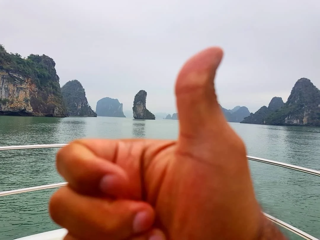 Cruising with Danny and Peter, Holland America Line, Westerdam, Halong Bay, Vietnam | A stunning view of the Hạ Long Bay Yacht cruising through emerald waters, surrounded by majestic limestone karsts. Guests enjoy Vietnamese seafood dining on the deck while kayaking in Hạ Long Bay. The private yacht tour showcases the beauty of this UNESCO World Heritage site.
