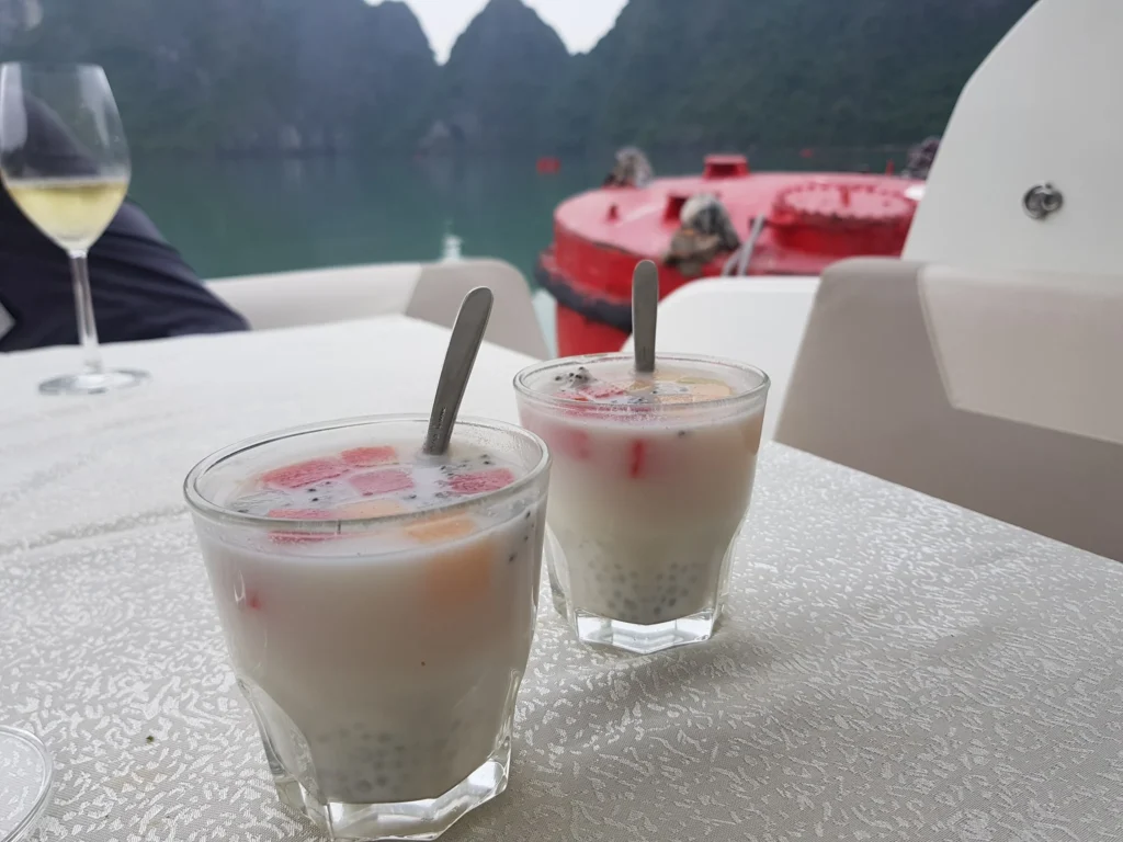 Cruising with Danny and Peter, Holland America Line, Westerdam, Halong Bay, Vietnam | A stunning view of the Hạ Long Bay Yacht cruising through emerald waters, surrounded by majestic limestone karsts. Guests enjoy Vietnamese seafood dining on the deck while kayaking in Hạ Long Bay. The private yacht tour showcases the beauty of this UNESCO World Heritage site.