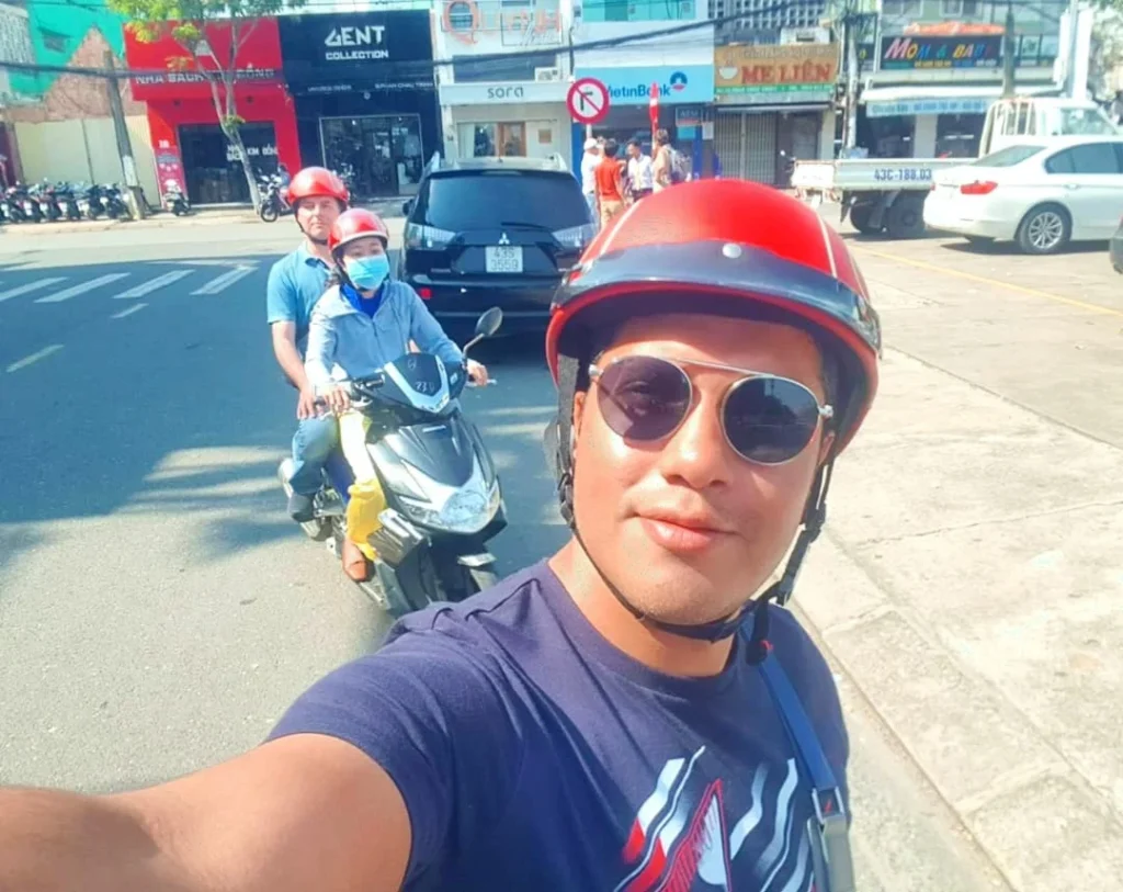 Cruising with Danny and Peter, Holland America Line, Westerdam, Da Nang, Hue, Vietnam | A vibrant street scene in Đà Nẵng showcasing a bustling market filled with fresh produce and aromatic spices, capturing the essence of Vietnamese cuisine. Motorbikes are parked nearby, symbolizing the thrilling motorbike street food tour. An enticing plate of bánh mì and bowls of pho are featured prominently, representing the local street eats enjoyed during this culinary exploration.