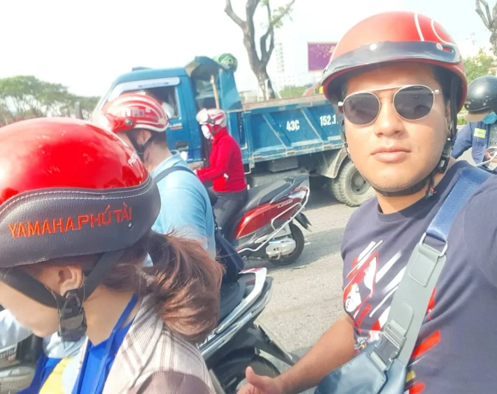 Cruising with Danny and Peter, Holland America Line, Westerdam, Da Nang, Hue, Vietnam | A vibrant street scene in Đà Nẵng showcasing a bustling market filled with fresh produce and aromatic spices, capturing the essence of Vietnamese cuisine. Motorbikes are parked nearby, symbolizing the thrilling motorbike street food tour. An enticing plate of bánh mì and bowls of pho are featured prominently, representing the local street eats enjoyed during this culinary exploration.