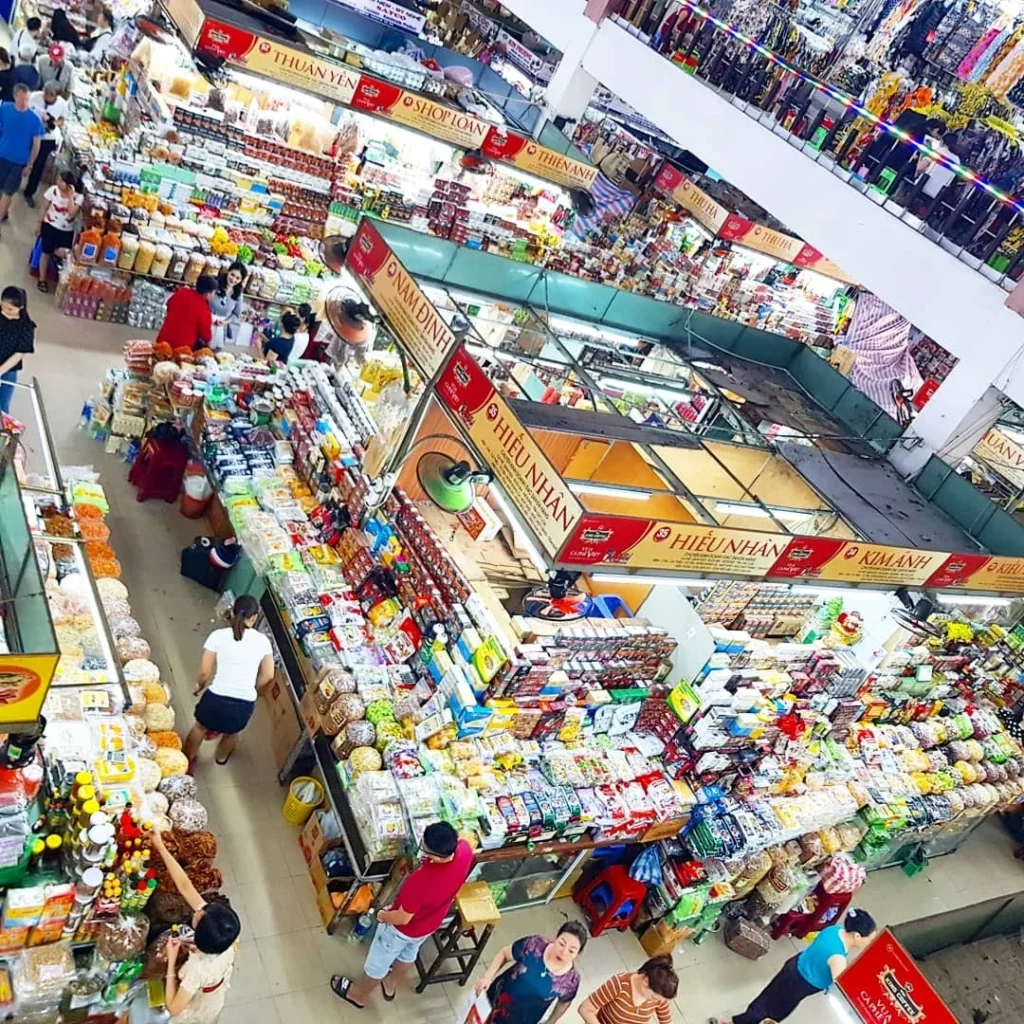 Cruising with Danny and Peter, Holland America Line, Westerdam, Da Nang, Hue, Vietnam | A vibrant street scene in Đà Nẵng showcasing a bustling market filled with fresh produce and aromatic spices, capturing the essence of Vietnamese cuisine. Motorbikes are parked nearby, symbolizing the thrilling motorbike street food tour. An enticing plate of bánh mì and bowls of pho are featured prominently, representing the local street eats enjoyed during this culinary exploration.