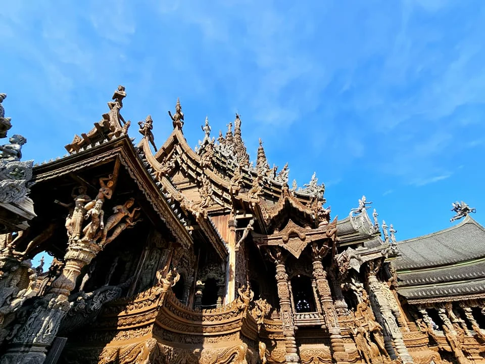 Cruising with Danny and Peter, Holland America Line, Westerdam, Laem Chabang, Bangkok, Thailand, Sanctuary Of Truth Pattaya Wonders | "Facade of the Sanctuary of Truth Pattaya showcasing intricate Thai Craftsmanship Art with towering wooden spires against a lush coastal backdrop, featuring detailed wooden carvings inside the Wooden Temple Pattaya depicting Buddhist Hindu Architecture and mythological scenes. The central hall houses a majestic wooden sculpture of a celestial deity, a highlight of Spiritual Sites Thailand and Thai Cultural Heritage. The luxurious Holland America Westerdam docked at Laem Chabang offers a Laem Chabang Excursion to explore Pattaya Cultural Landmarks, while lush greenery surrounds this Pattaya Tourist Attraction inspired by Ayutthaya Kingdom Design.