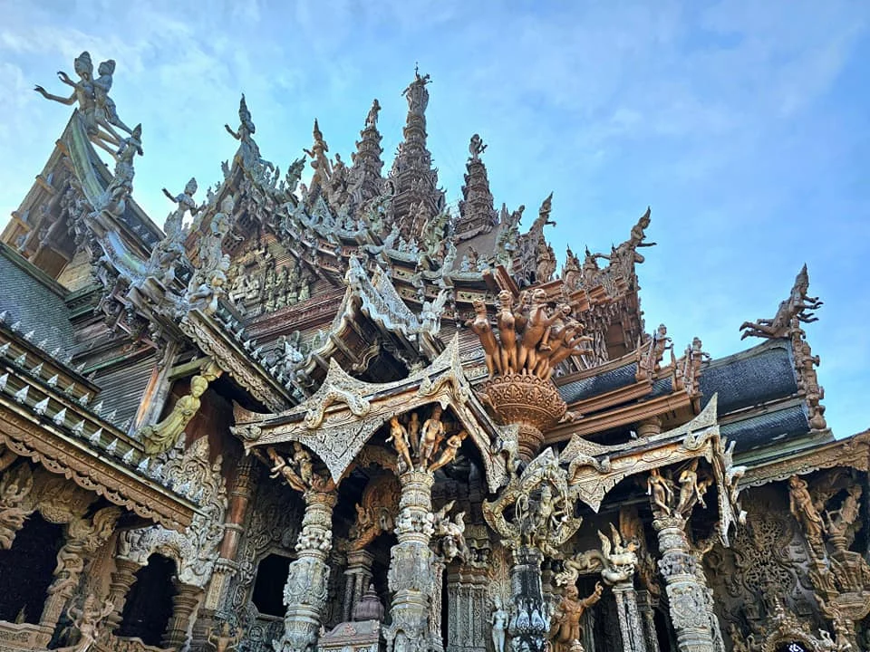 Cruising with Danny and Peter, Holland America Line, Westerdam, Laem Chabang, Bangkok, Thailand, Sanctuary Of Truth Pattaya Wonders | "Facade of the Sanctuary of Truth Pattaya showcasing intricate Thai Craftsmanship Art with towering wooden spires against a lush coastal backdrop, featuring detailed wooden carvings inside the Wooden Temple Pattaya depicting Buddhist Hindu Architecture and mythological scenes. The central hall houses a majestic wooden sculpture of a celestial deity, a highlight of Spiritual Sites Thailand and Thai Cultural Heritage. The luxurious Holland America Westerdam docked at Laem Chabang offers a Laem Chabang Excursion to explore Pattaya Cultural Landmarks, while lush greenery surrounds this Pattaya Tourist Attraction inspired by Ayutthaya Kingdom Design.