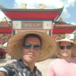 Cruising with Danny and Peter, Holland America Line, Westerdam, Laem Chabang, Bangkok, Thailand | A serene view of Wat Yan Nasangwararam temple in Pattaya, showcasing intricate Thai architecture surrounded by lush greenery. In the foreground, worshippers engage in meditation and tranquility, while the majestic Khao Chi Chan Buddha monument looms in the background, radiating serenity. This scene captures the essence of a spiritual journey in Pattaya, highlighting the cultural heritage of Thai Buddhism and the beauty of religious art in Thailand.