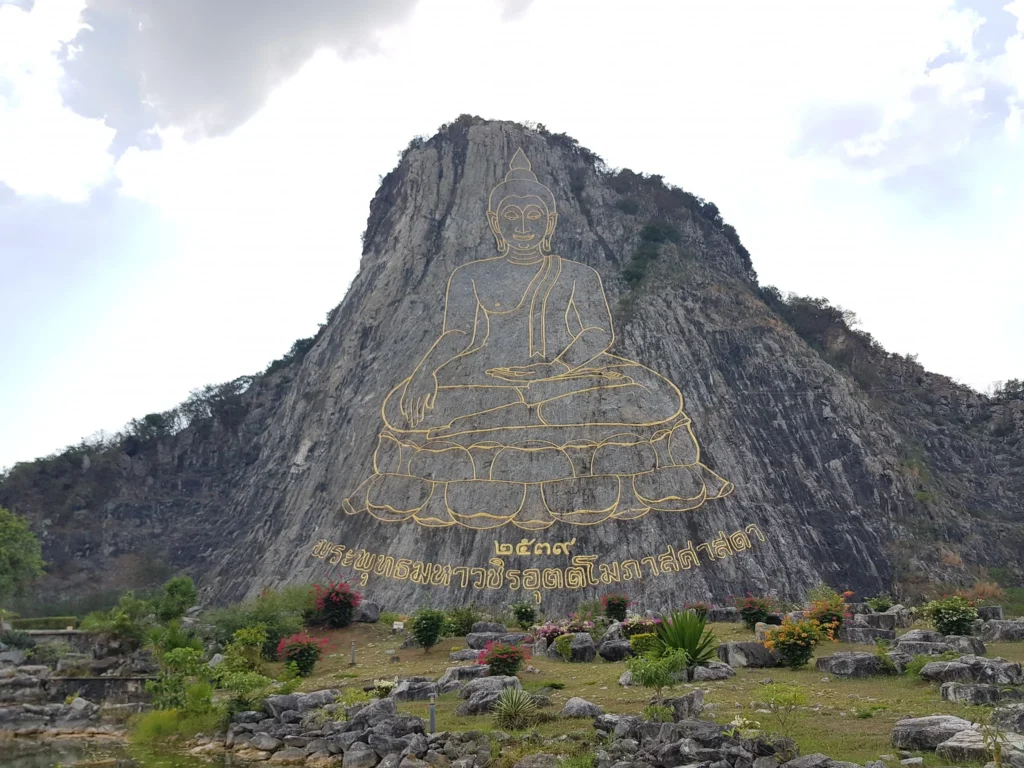 Cruising with Danny and Peter, Holland America Line, Westerdam, Laem Chabang, Bangkok, Thailand | A serene view of Wat Yan Nasangwararam temple in Pattaya, showcasing intricate Thai architecture surrounded by lush greenery. In the foreground, worshippers engage in meditation and tranquility, while the majestic Khao Chi Chan Buddha monument looms in the background, radiating serenity. This scene captures the essence of a spiritual journey in Pattaya, highlighting the cultural heritage of Thai Buddhism and the beauty of religious art in Thailand.