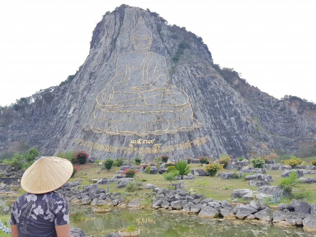 Cruising with Danny and Peter, Holland America Line, Westerdam, Laem Chabang, Bangkok, Thailand | A serene view of Wat Yan Nasangwararam temple in Pattaya, showcasing intricate Thai architecture surrounded by lush greenery. In the foreground, worshippers engage in meditation and tranquility, while the majestic Khao Chi Chan Buddha monument looms in the background, radiating serenity. This scene captures the essence of a spiritual journey in Pattaya, highlighting the cultural heritage of Thai Buddhism and the beauty of religious art in Thailand.