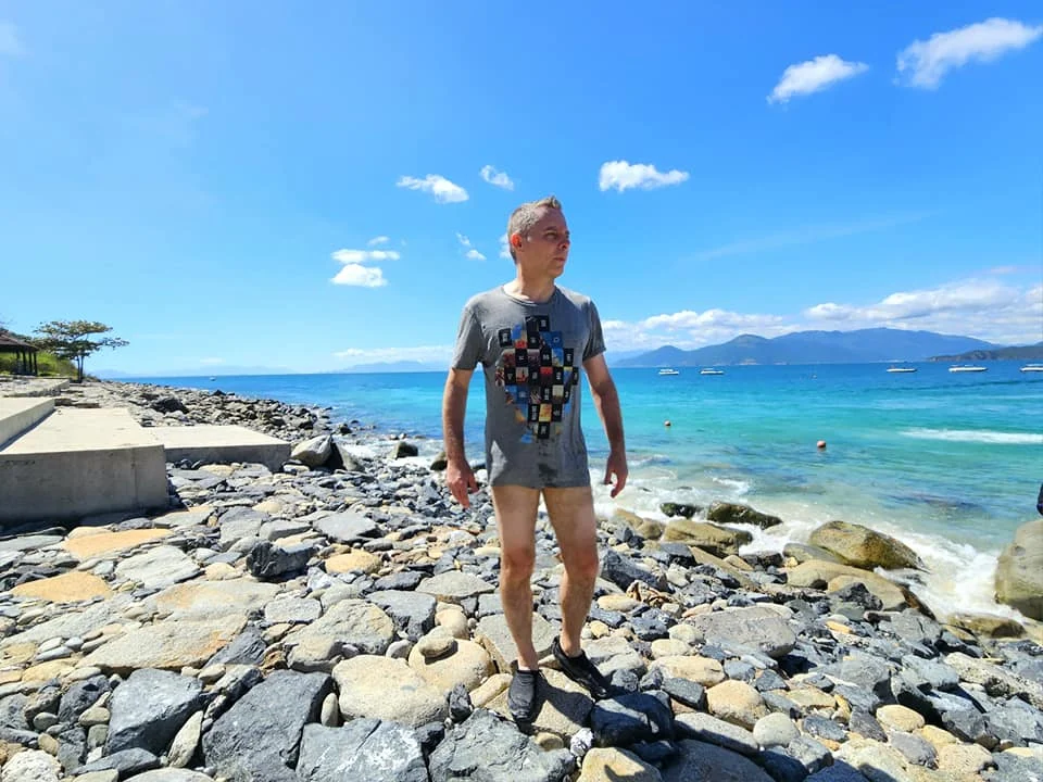 Cruising with Danny and Peter, Holland America Line, Westerdam, Nha Trang, Vietnam, Nha Trang Island Escapade Adventure | Group of tourists enjoying a Nha Trang Island Escapade Adventure featuring Mieu Island Exploration under a tropical sun, vibrant underwater scenes from Coral Reef Snorkeling in Nha Trang Bay, the pirate ship-shaped Tri Nguyen Aquarium showcasing a Marine Life Experience on a Vietnam Coastal Adventure, local fishermen feeding groupers during a Fishing Village Visit, relaxing on golden sands at Mini Beach Relaxation after a Nha Trang Island Tour with Holland America Cruise, and a scenic view of Nha Trang Bay from a boat during a Tropical Island Retreat.