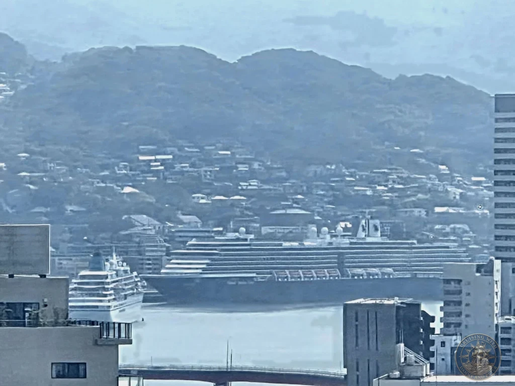 Panoramic view from the Nagasaki Ferris wheel showing two large cruise ships docked in Nagasaki harbor, with city buildings, bridges, and green mountains in the background — featured in Nagasaki Japan cruise port guide. Ideal for things to do in Nagasaki from cruise ship and one day in Nagasaki Japan itinerary from the Westerdam docking location by Danny and Peter.
