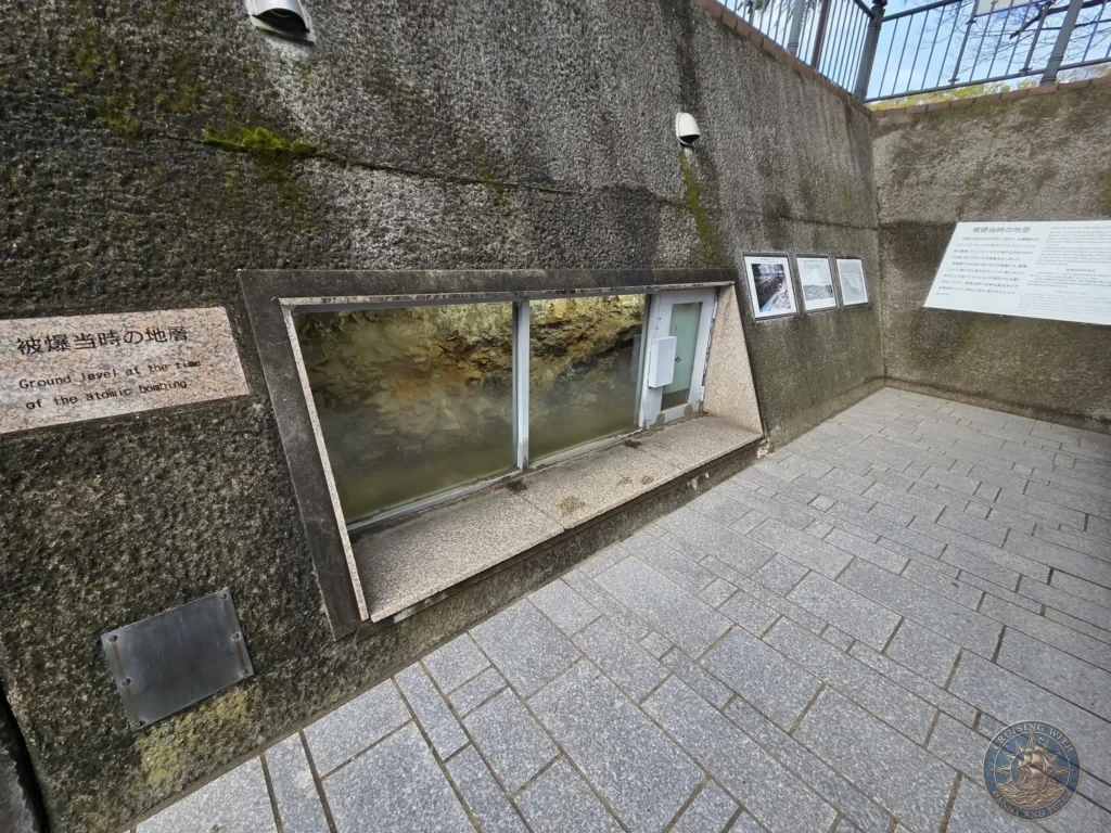 Preserved ground level window at the Hypocenter Park in Nagasaki, Japan, showing the exact earth and rubble from the moment of the 1945 atomic bombing. Informational signs in Japanese and English explain the site. Featured in Nagasaki Japan cruise port guide, things to do in Nagasaki from cruise ship, and one day in Nagasaki Japan itinerary from the Westerdam. by Danny and Peter.