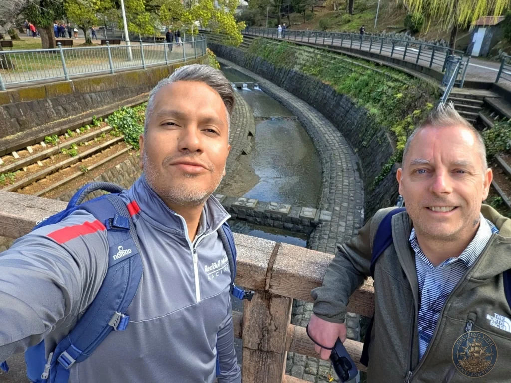 Selfie of Danny and Peter at Hypocenter Park in Nagasaki, Japan, standing on a wooden bridge overlooking the historic stone canal. The peaceful park setting includes stone walls, greenery, and pathways near the atomic bombing epicenter. Featured in Nagasaki Japan cruise port guide, things to do in Nagasaki from cruise ship, and one day in Nagasaki Japan itinerary from the Westerdam. by Danny and Peter.