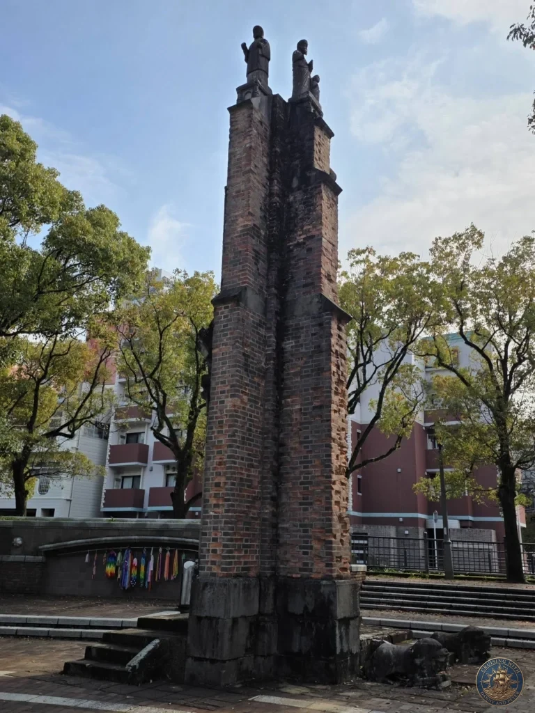Tall brick ruins of Urakami Cathedral with two statues of saints on top, located at Hypocenter Park in Nagasaki, Japan. The surviving structure from the 1945 atomic bombing stands as a powerful memorial. Featured in Nagasaki Japan cruise port guide, things to do in Nagasaki from cruise ship, and one day in Nagasaki Japan itinerary from the Westerdam. by Danny and Peter.