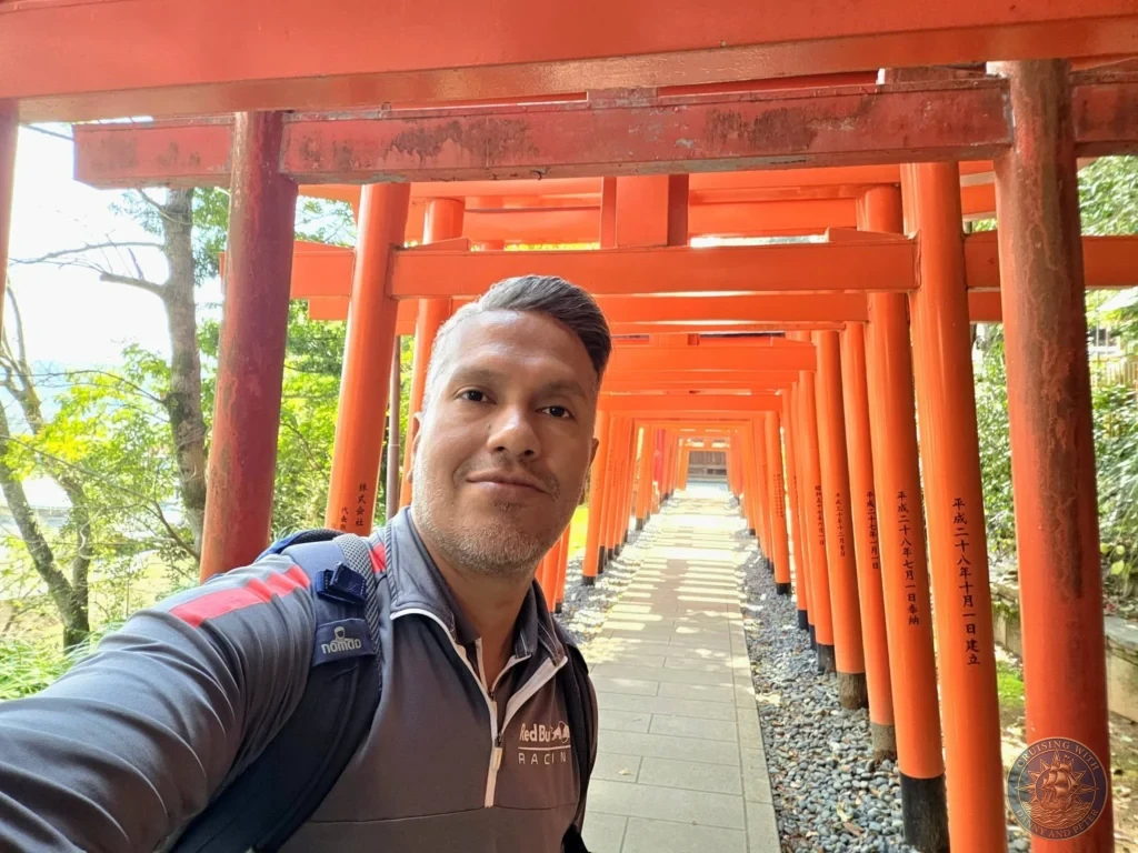 Selfie of Danny inside the long tunnel of red torii gates at Suwa Shrine in Nagasaki, Japan. The vibrant orange gates line the path on both sides, creating a striking corridor with trees visible in the background. Featured in Nagasaki Japan cruise port guide, things to do in Nagasaki from cruise ship, and one day in Nagasaki Japan itinerary from the Westerdam. by Danny and Peter.