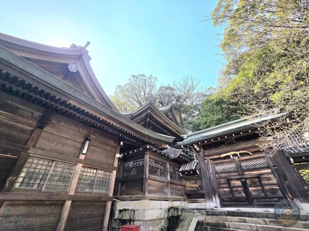 Traditional wooden shrine buildings with dark tiled roofs at Suwa Shrine in Nagasaki, Japan. The architecture features ornate details and is surrounded by lush green trees under a clear blue sky. Featured in Nagasaki Japan cruise port guide, things to do in Nagasaki from cruise ship, and one day in Nagasaki Japan itinerary from the Westerdam. by Danny and Peter.