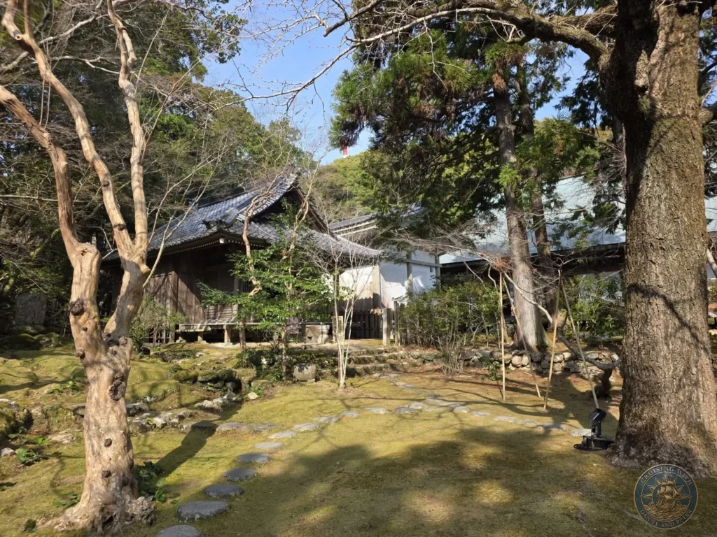 Scenic temple grounds with traditional wooden buildings, stone paths, and lush trees at Chikurin Temple in Kochi, Japan. Peaceful forested setting with mossy garden elements. Kochi Cruise Port Guide | Things to do in Kochi from cruise ship | One day in Kochi Japan itinerary by Danny and Peter.