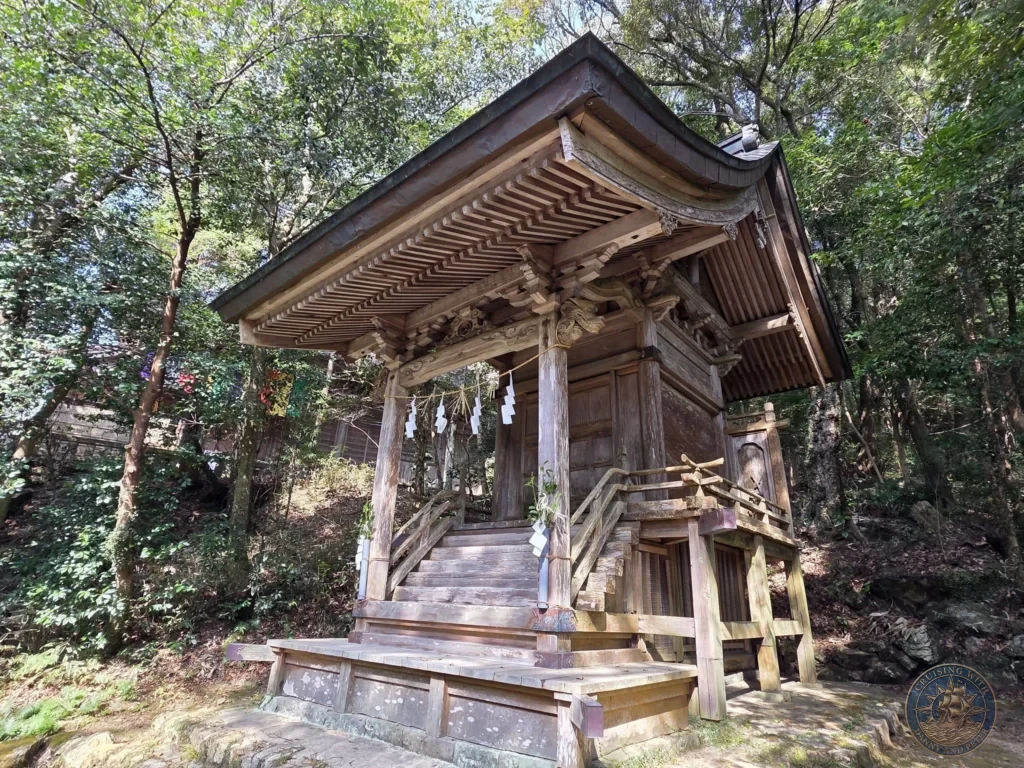Charming wooden shrine building on a raised platform with detailed carvings at Chikurin Temple in Kochi, Japan. Peaceful forest setting with traditional architecture. Kochi Cruise Port Guide | Things to do in Kochi from cruise ship | One day in Kochi Japan itinerary by Danny and Peter.