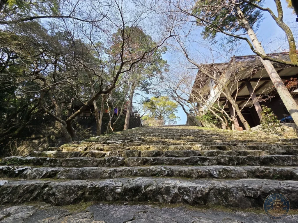 Dramatic long stone staircase leading up through the forest at Chikurin Temple in Kochi, Japan. Scenic tree-lined path with traditional temple buildings in the background. Kochi Cruise Port Guide | Things to do in Kochi from cruise ship | One day in Kochi Japan itinerary by Danny and Peter.