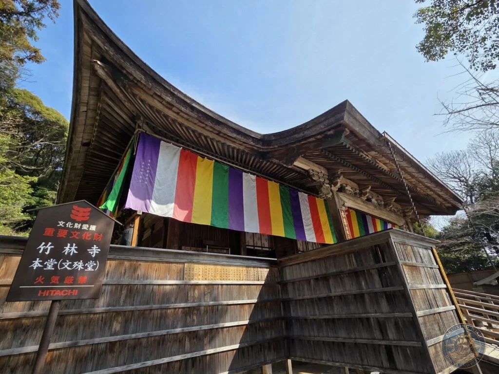 Traditional wooden main hall with colorful prayer flags at Chikurin Temple (Bamboo Forest Temple) in Kochi, Japan. Ornate roof and historic temple architecture. Kochi Cruise Port Guide | Things to do in Kochi from cruise ship | One day in Kochi Japan itinerary by Danny and Peter.