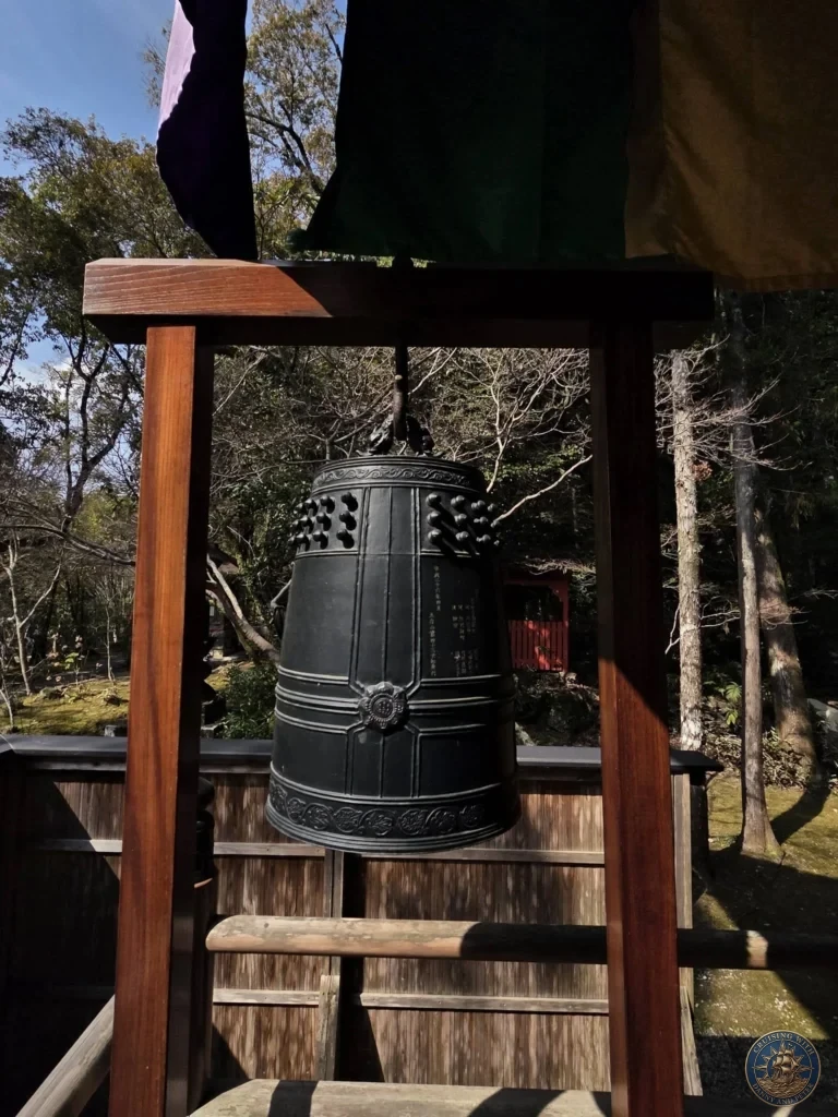 Large bronze temple bell hanging in a traditional wooden frame at Chikurin Temple in Kochi, Japan. Historic bell with inscriptions surrounded by forest. Kochi Cruise Port Guide | Things to do in Kochi from cruise ship | One day in Kochi Japan itinerary by Danny and Peter.