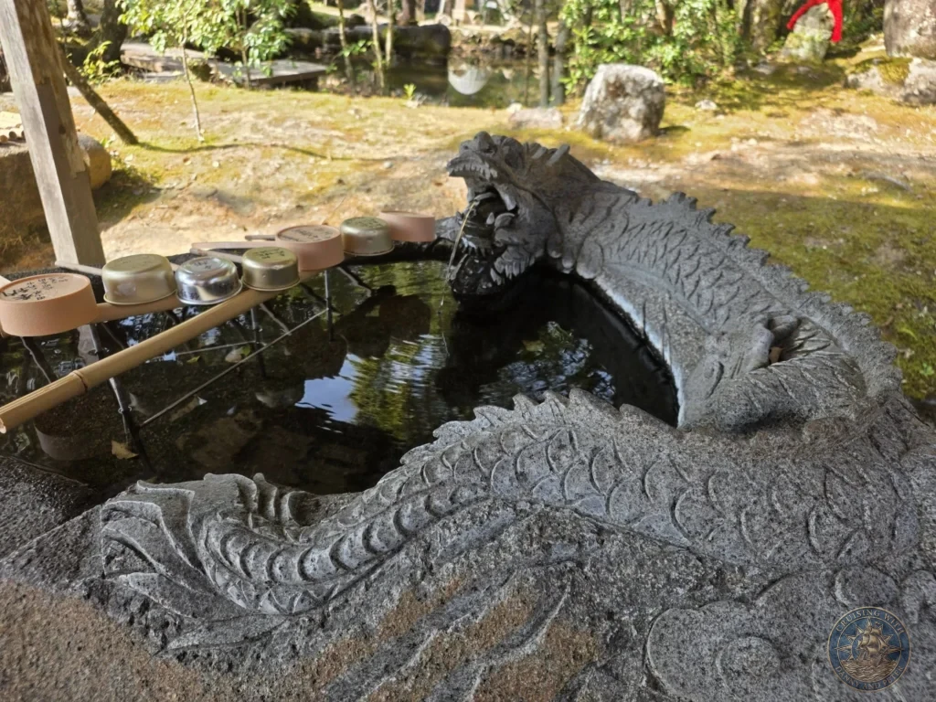 Stone dragon fountain with water flowing from its mouth into a basin at Chikurin Temple in Kochi, Japan. Traditional purification feature with metal cups for visitors. Kochi Cruise Port Guide | Things to do in Kochi from cruise ship | One day in Kochi Japan itinerary by Danny and Peter.