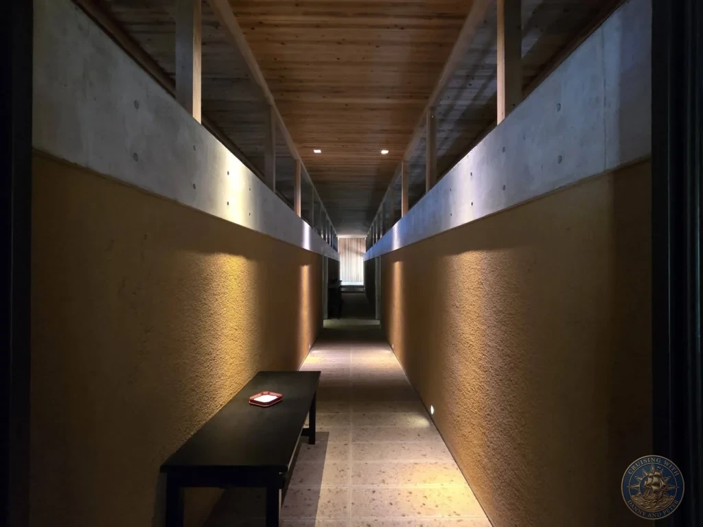 Long modern hallway with concrete walls, wooden ceiling, and warm lighting at Chikurin Temple in Kochi, Japan. Contemporary architecture within the historic temple complex. Kochi Cruise Port Guide | Things to do in Kochi from cruise ship | One day in Kochi Japan itinerary by Danny and Peter.