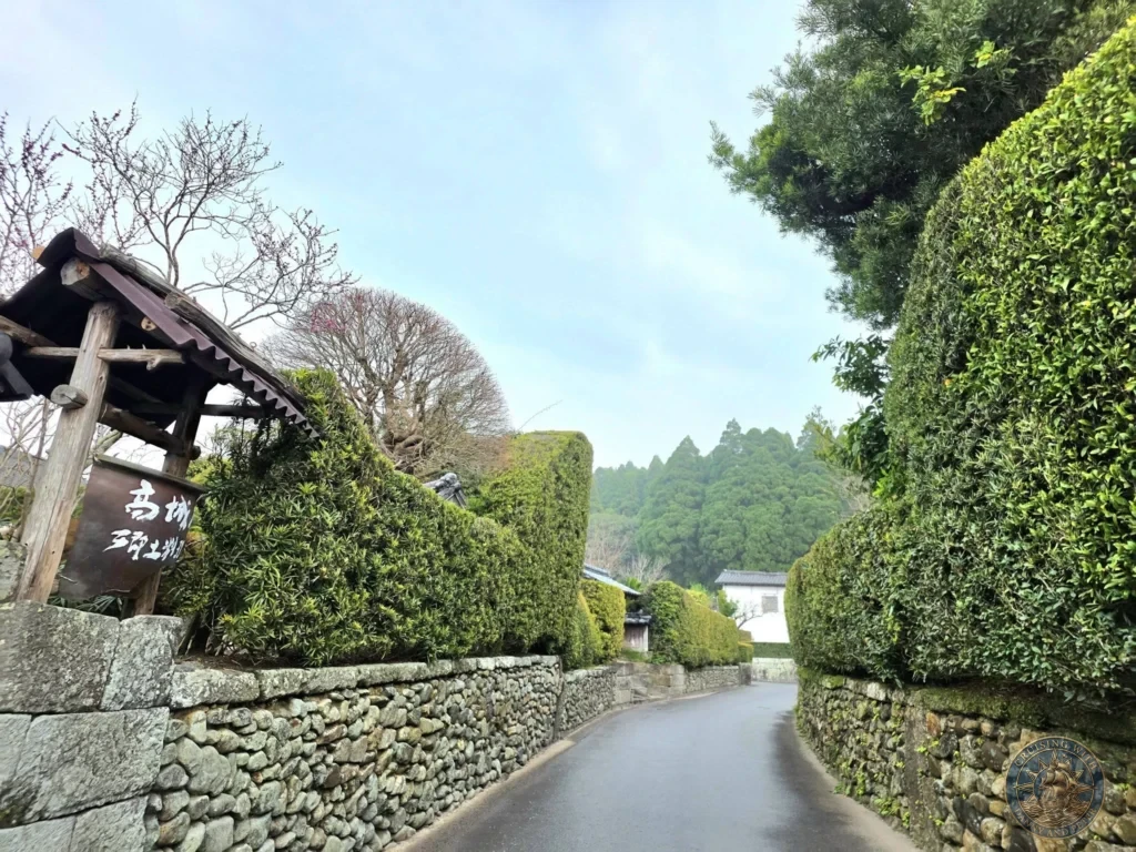 Charming curved path lined with traditional stone walls and tall manicured hedges in the historic Chiran Samurai District. Beautiful view of preserved samurai residences and lush greenery in Kagoshima, Japan. Kagoshima Cruise Port Guide | Things to do in Kagoshima from cruise ship | One day in Kagoshima Japan itinerary by Danny and Peter.