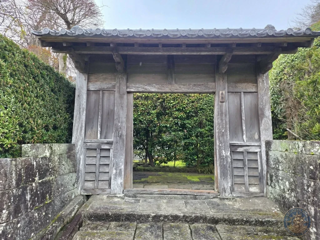 Front view of a traditional wooden samurai residence gate with tiled roof and stone steps leading into a lush garden in Chiran Samurai District. Iconic preserved Edo-period architecture and scenery in Kagoshima, Japan. Kagoshima Cruise Port Guide | Things to do in Kagoshima from cruise ship | One day in Kagoshima Japan itinerary by Danny and Peter.
