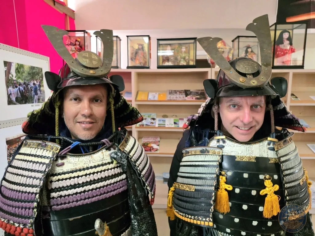 Danny and Peter smiling in full traditional samurai armor at the Chiran Doll & Toy Museum gift shop in Kagoshima. Fun hands-on activity while visiting the historic Chiran Samurai District. Kagoshima Cruise Port Guide | Things to do in Kagoshima from cruise ship | One day in Kagoshima Japan itinerary by Danny and Peter.