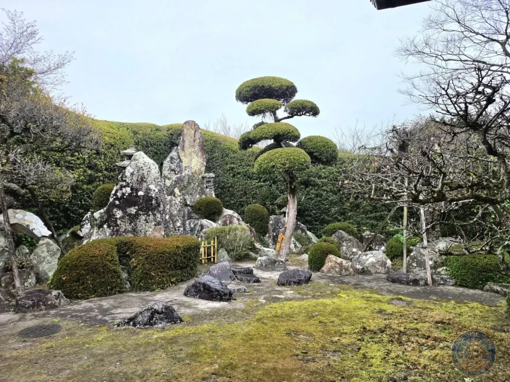Stunning dry landscape rock garden with moss-covered stones, dramatic rock formations, and iconic cloud-pruned trees in Sata Shigetada Garden (Garden 6) at the Chiran Samurai District. Beautiful traditional Japanese garden in Kagoshima, Japan. Kagoshima Cruise Port Guide | Things to do in Kagoshima from cruise ship | One day in Kagoshima Japan itinerary by Danny and Peter.