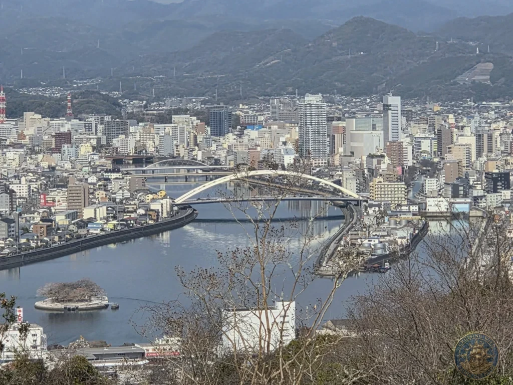 Breathtaking panoramic view of Kochi city, river, iconic bridge, harbor, and mountains from Godaisan Observatory in Kochi, Japan. Stunning scenic overlook. Kochi Cruise Port Guide | Things to do in Kochi from cruise ship | One day in Kochi Japan itinerary by Danny and Peter.