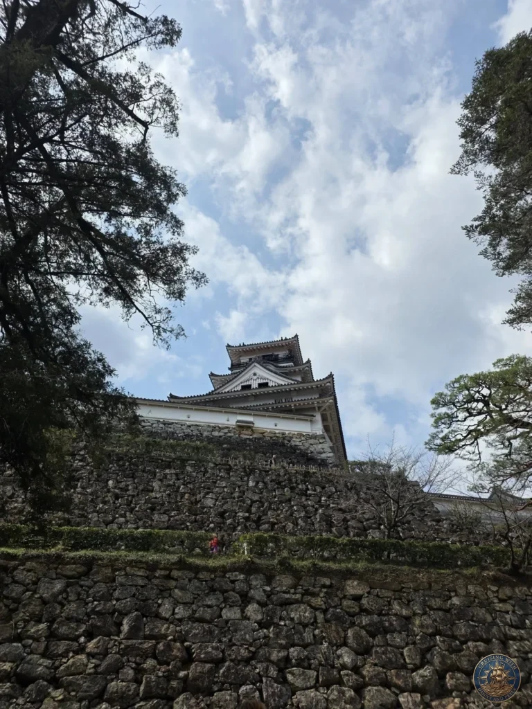 Dramatic low-angle view of Kochi Castle keep towering above stone walls and framed by trees in Kochi, Japan. Iconic historic Japanese castle. Kochi Cruise Port Guide | Things to do in Kochi from cruise ship | One day in Kochi Japan itinerary by Danny and Peter.