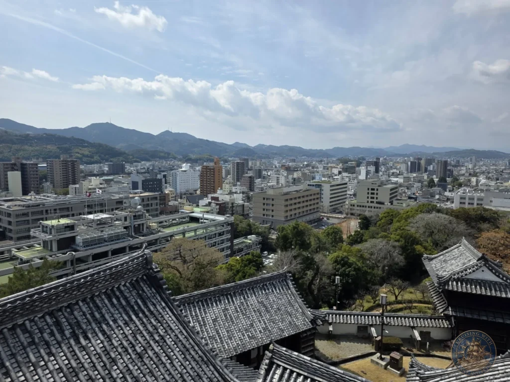 Panoramic view from Kochi Castle overlooking the city rooftops, modern buildings, and surrounding mountains in Kochi, Japan. Scenic overlook from historic landmark. Kochi Cruise Port Guide | Things to do in Kochi from cruise ship | One day in Kochi Japan itinerary by Danny and Peter.