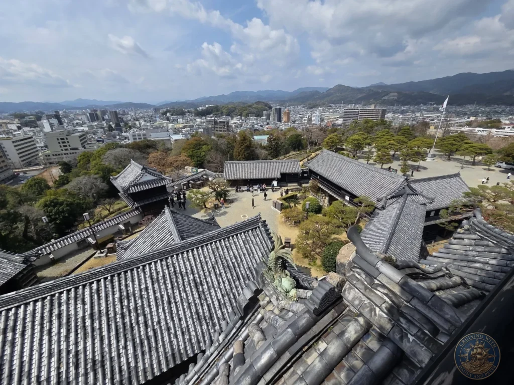 High-angle panoramic view from Kochi Castle keep overlooking the castle grounds, traditional roofs, city, and mountains in Kochi, Japan. Scenic historic overlook. Kochi Cruise Port Guide | Things to do in Kochi from cruise ship | One day in Kochi Japan itinerary by Danny and Peter.