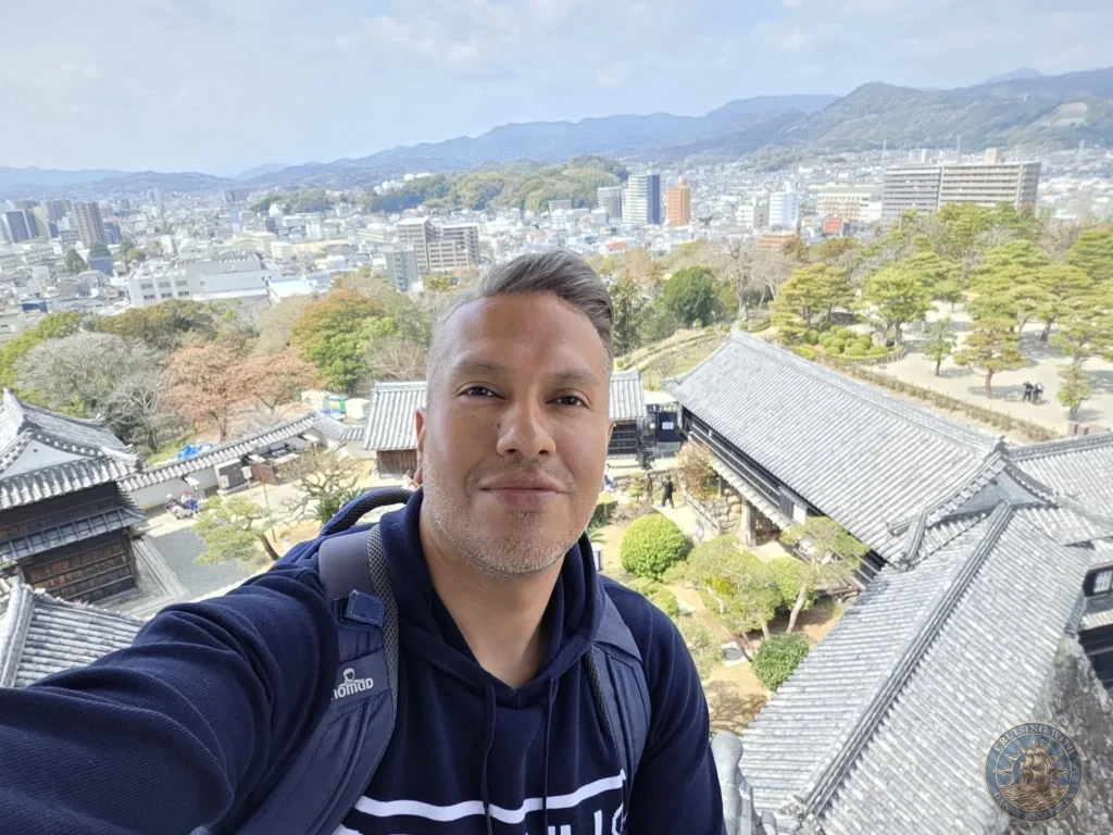Danny taking a selfie from the top of Kochi Castle with sweeping panoramic views of the city and mountains in Kochi, Japan. Iconic historic viewpoint. Kochi Cruise Port Guide | Things to do in Kochi from cruise ship | One day in Kochi Japan itinerary by Danny and Peter.
