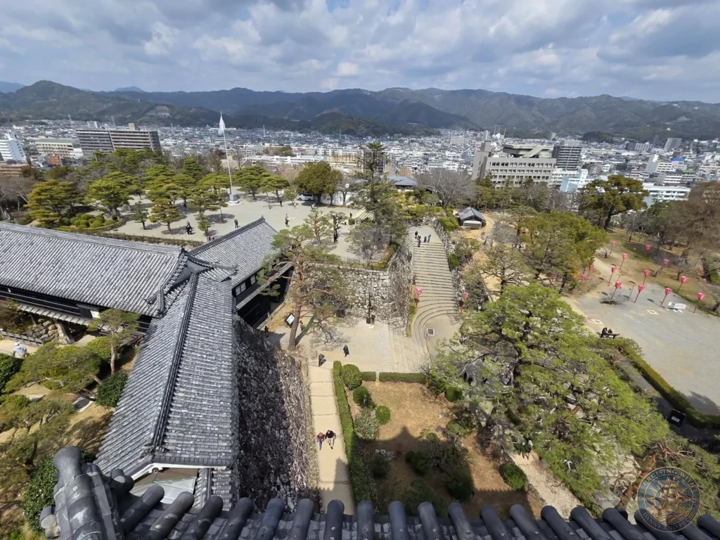 High-angle panoramic view from Kochi Castle overlooking the castle grounds, traditional buildings, modern city, and mountains in Kochi, Japan. Scenic historic overlook. Kochi Cruise Port Guide | Things to do in Kochi from cruise ship | One day in Kochi Japan itinerary by Danny and Peter.