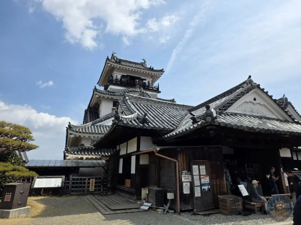 Kochi Castle keep and traditional wooden structures on the castle grounds under a blue sky in Kochi, Japan. Historic Japanese castle complex. Kochi Cruise Port Guide | Things to do in Kochi from cruise ship | One day in Kochi Japan itinerary by Danny and Peter.
