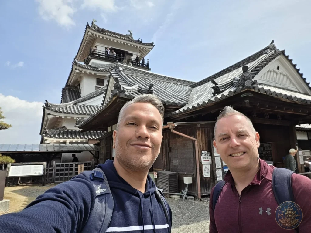 Danny and Peter taking a selfie with Kochi Castle buildings in the background in Kochi, Japan. Historic landmark under a blue sky. Kochi Cruise Port Guide | Things to do in Kochi from cruise ship | One day in Kochi Japan itinerary by Danny and Peter.