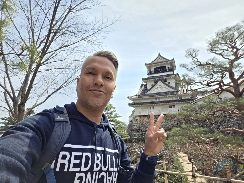 Danny taking a selfie with Kochi Castle keep in the background in Kochi, Japan. Historic white castle surrounded by trees. Kochi Cruise Port Guide | Things to do in Kochi from cruise ship | One day in Kochi Japan itinerary by Danny and Peter.