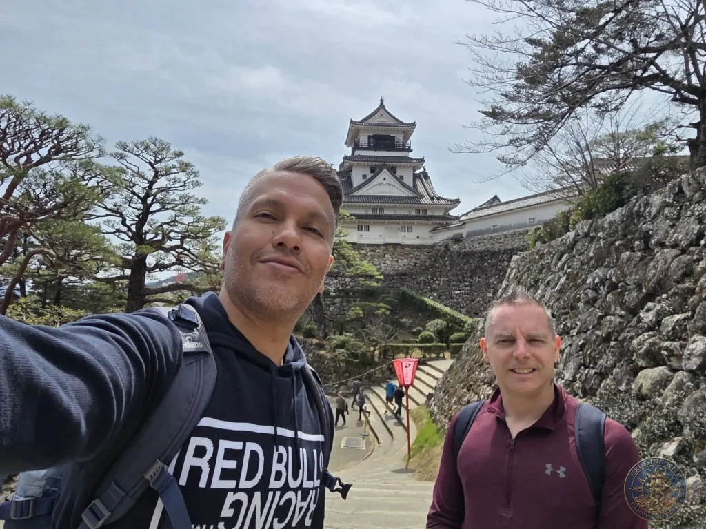 Danny and Peter taking a selfie on the stone stairs leading up to Kochi Castle with the historic keep in the background in Kochi, Japan. Kochi Cruise Port Guide | Things to do in Kochi from cruise ship | One day in Kochi Japan itinerary by Danny and Peter.