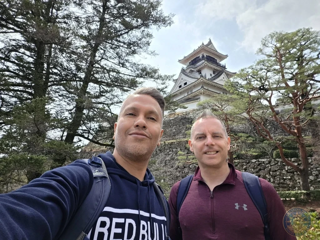 Danny and Peter taking a selfie with the iconic Kochi Castle keep in the background framed by trees in Kochi, Japan. Historic landmark. Kochi Cruise Port Guide | Things to do in Kochi from cruise ship | One day in Kochi Japan itinerary by Danny and Peter.
