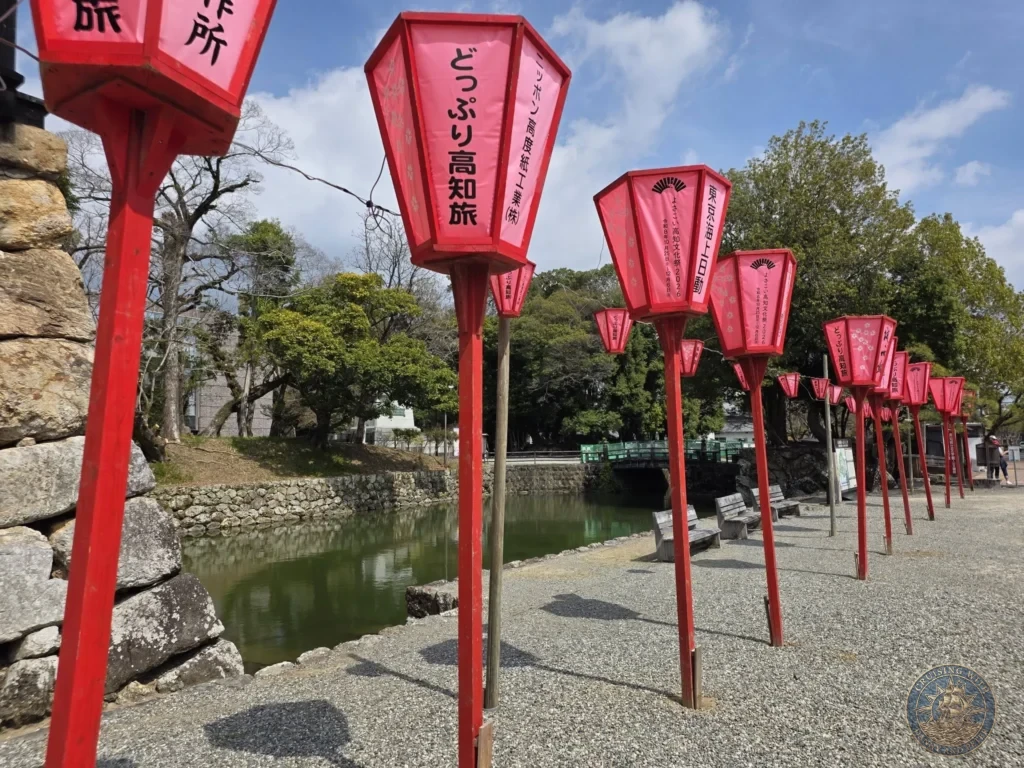 Row of bright red lanterns along the path near Kochi Castle in Kochi, Japan. Festive decorations with historic castle backdrop. Kochi Cruise Port Guide | Things to do in Kochi from cruise ship | One day in Kochi Japan itinerary by Danny and Peter.