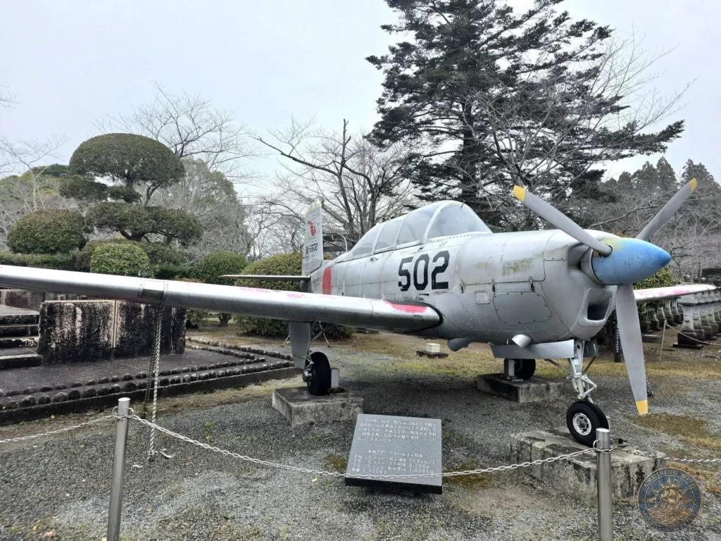 Preserved kamikaze training aircraft on display at the Chiran Peace Museum for Kamikaze Pilots, with informative plaque in front. Historic outdoor exhibit in the Chiran Samurai District, Kagoshima, Japan. Kagoshima Cruise Port Guide | Things to do in Kagoshima from cruise ship | One day in Kagoshima Japan itinerary by Danny and Peter.