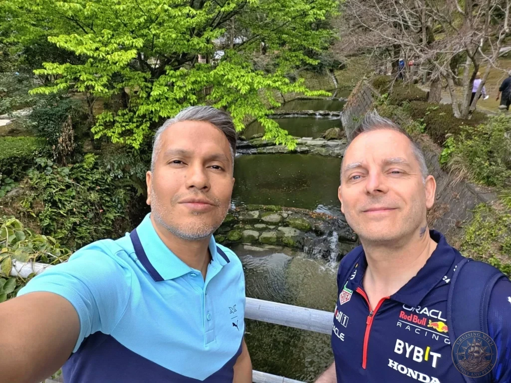 Danny and Peter taking a selfie at Sengan-en (Iso Garden) with lush green trees, a pond, and traditional landscaping in the background. Scenic spring views at the historic UNESCO World Heritage samurai garden in Kagoshima, Japan. Kagoshima Cruise Port Guide | Things to do in Kagoshima from cruise ship | One day in Kagoshima Japan itinerary by Danny and Peter.