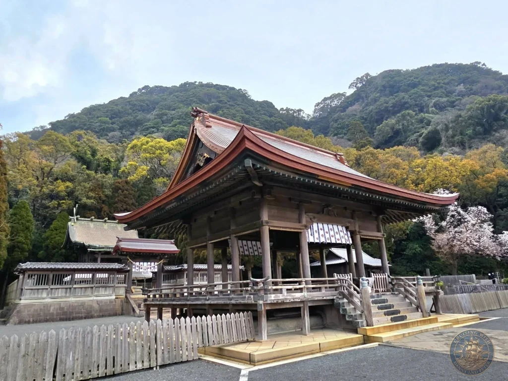 Historic Tsurugane Shrine with its elegant red roof and traditional wooden architecture at Sengan-en (Iso Garden), the UNESCO World Heritage samurai villa in Kagoshima, Japan. Scenic shrine nestled against forested hills. Kagoshima Cruise Port Guide | Things to do in Kagoshima from cruise ship | One day in Kagoshima Japan itinerary by Danny and Peter.